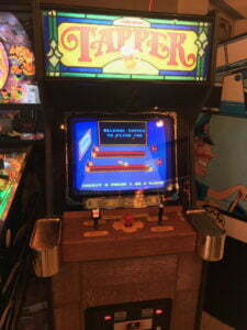 Tapper arcade cabinet with beer tap handle and brass drink holders on the side.